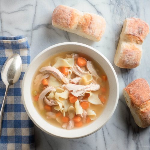 chicken noodle soup from scratch in white bowl with bread