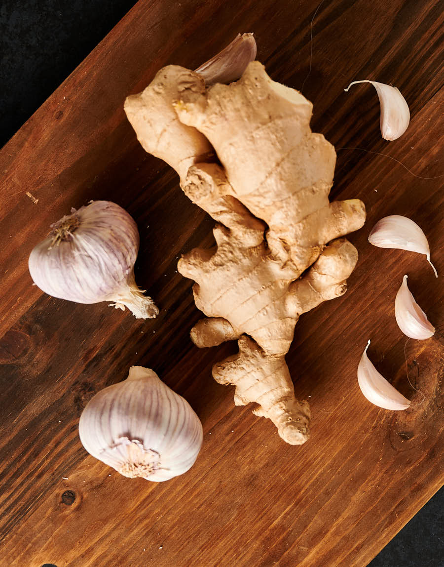 Heads and cloves of garlic and large ginger bulb of a cutting board from above.