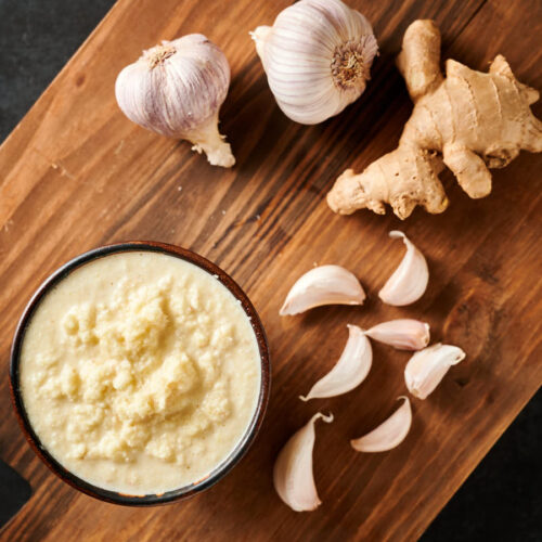 Bowl of fresh garlic ginger paste on a board with raw garlic and ginger from above.