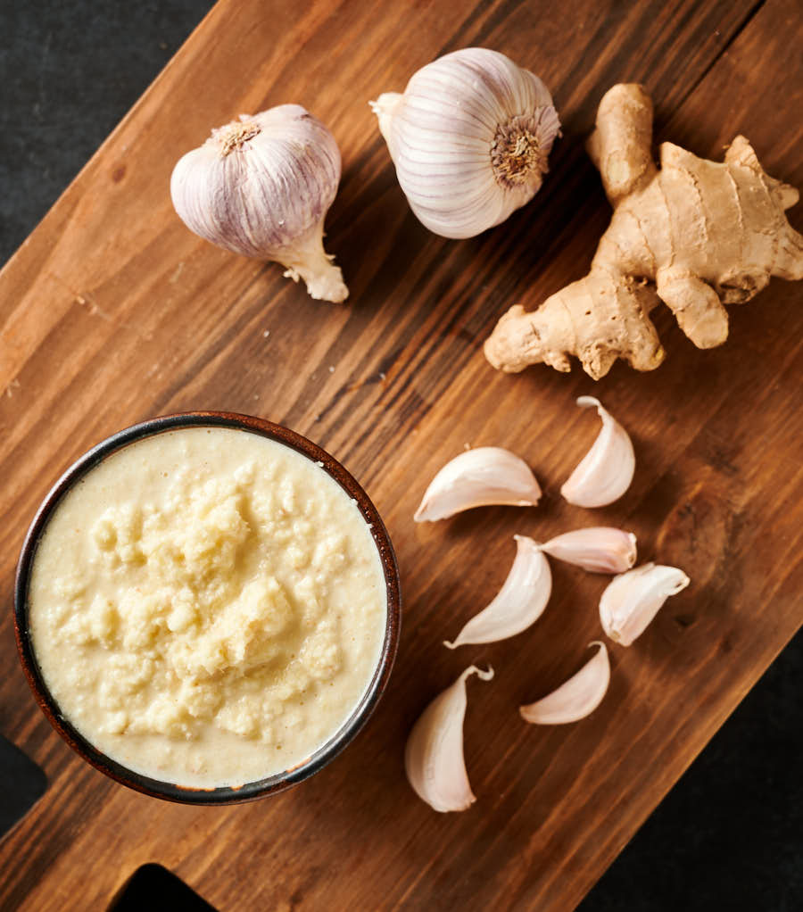 Bowl of fresh garlic ginger paste on a board with raw garlic and ginger from above.