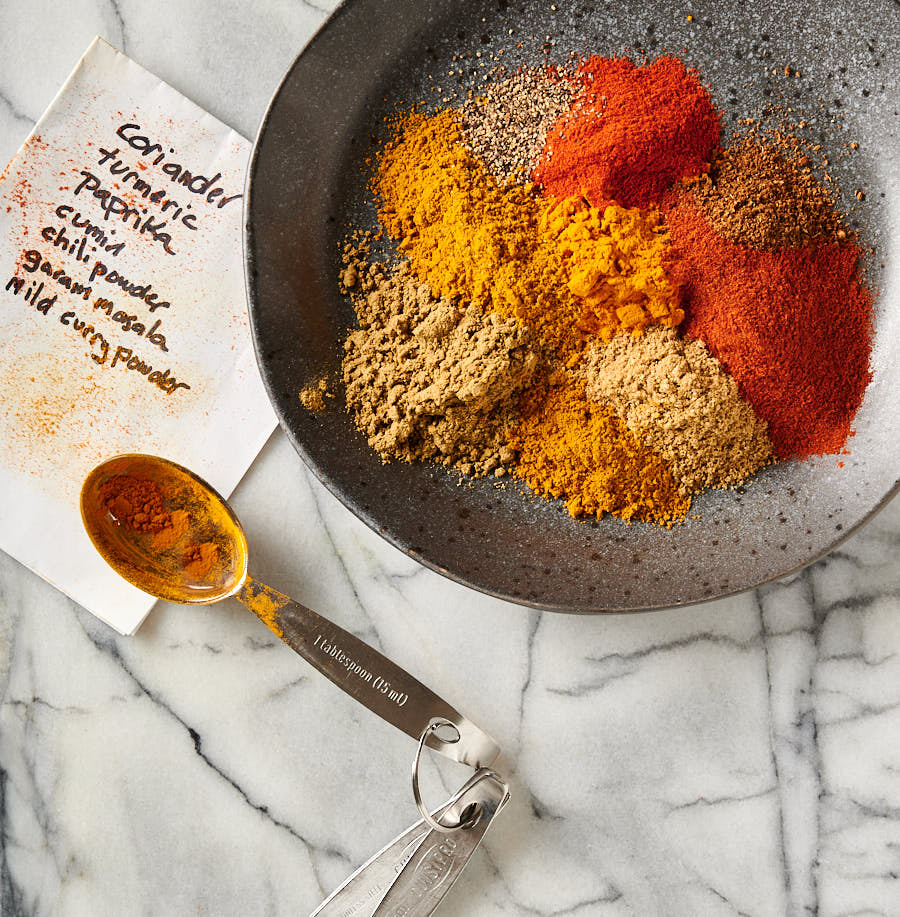 Individual spices on a plate with recipe card and measuring spoons.