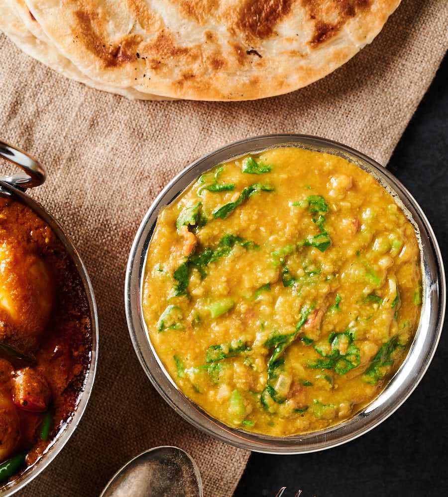 Table scene with lentil curry, egg curry and parathas from above.