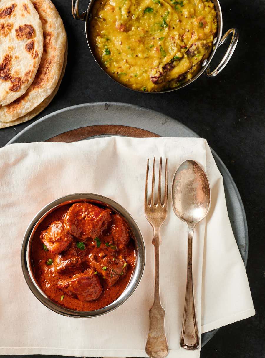 Chicken tikka masala, tarka dal and parathas table scene from above.