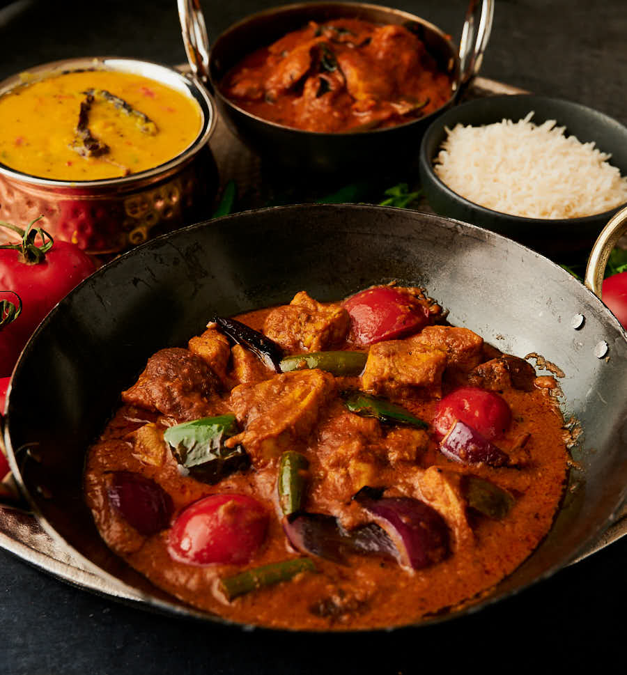 Front view of restaurant chicken jalfrezi with curries and rice in the background.