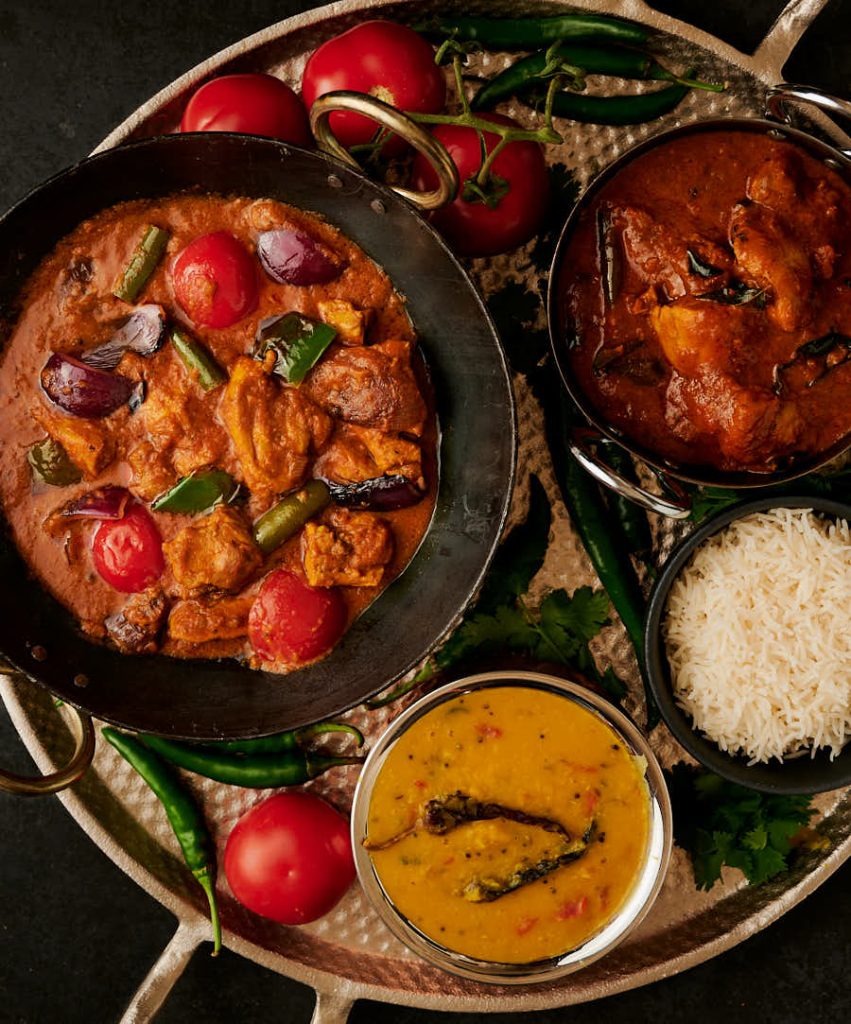 Chicken jalfrezi in a kadai surrounded by curries, dal and and rice.