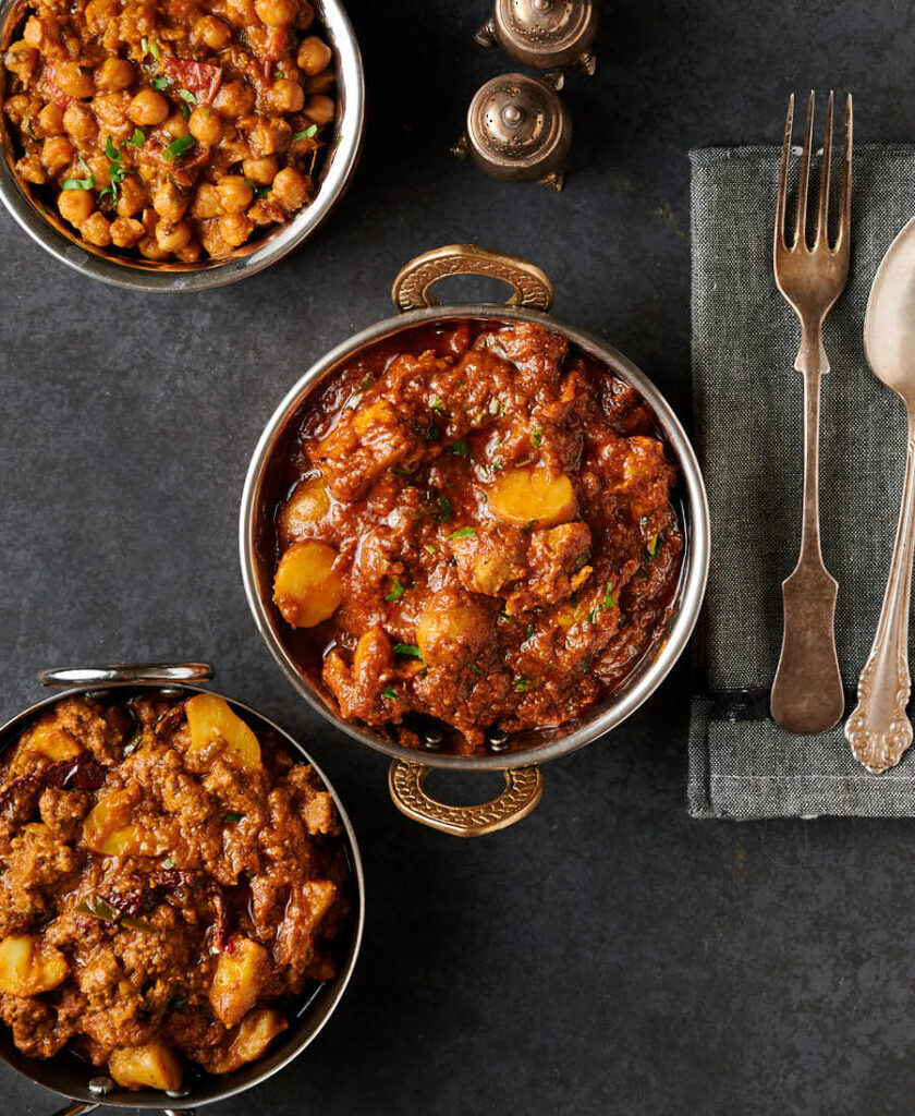 Aloo chicken curry surrounded by bowls of chana masala and beef keema.