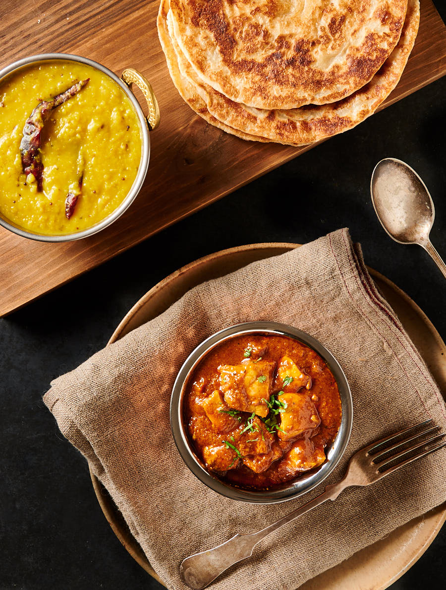 Table scene with restaurant style pathia curry, tarka dal and parathas from above