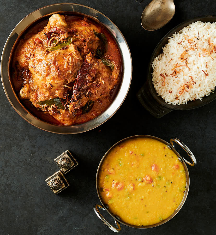 Table scene with chettinad chicken curry, dal and jeera rice from above.