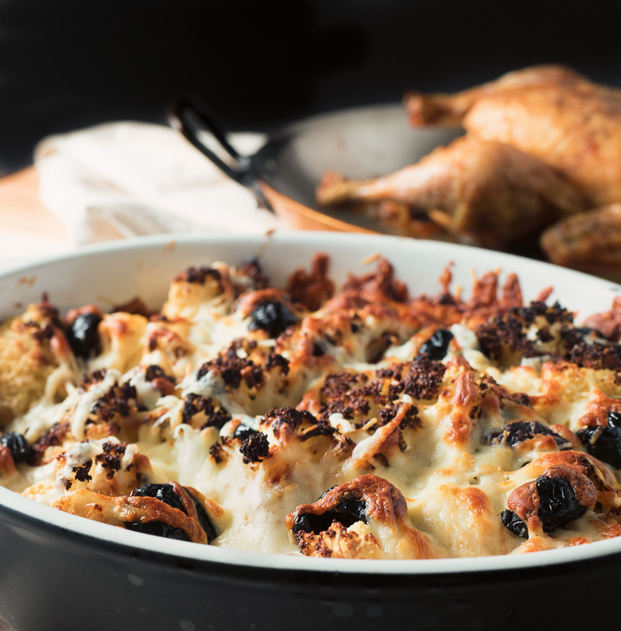 Roasted cauliflower gratin with browned melted cheese and olives front view.