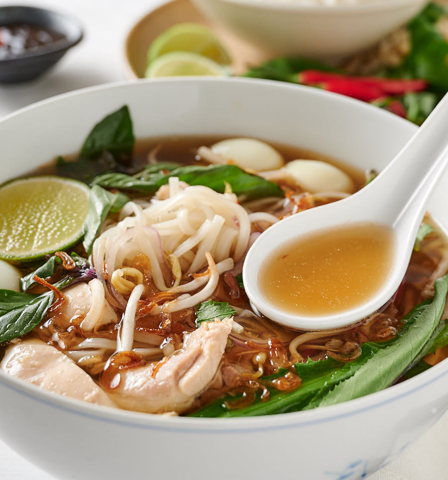 Spoonful of broth over bowl of pho ga.