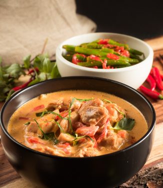 thai red chicken curry in a black bowl front view