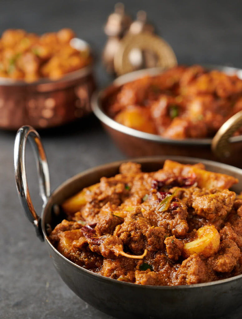 Bowl of aloo keema with chicken curry in the background. From the front.