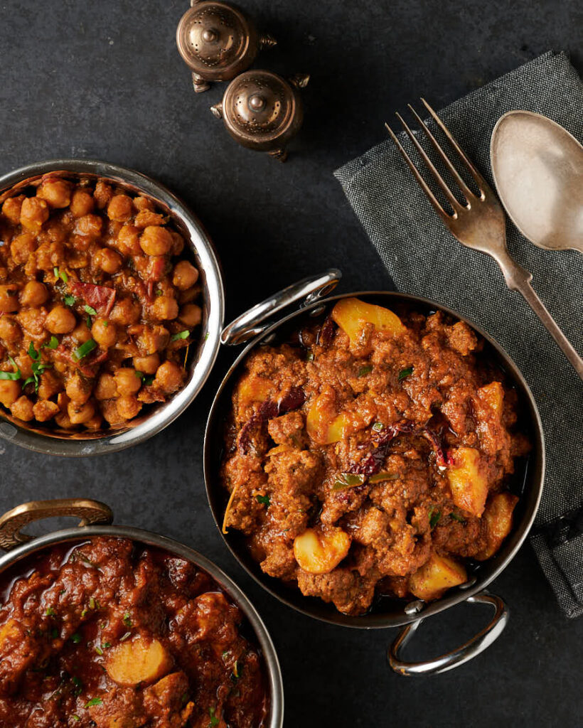 Aloo keema, chana masala and chicken chaat curry in serving bowls from above.