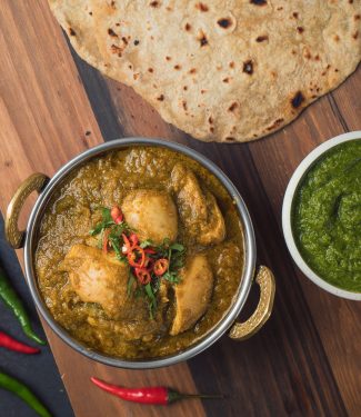 hariyali chicken curry in Indian copper bowl with chapati.