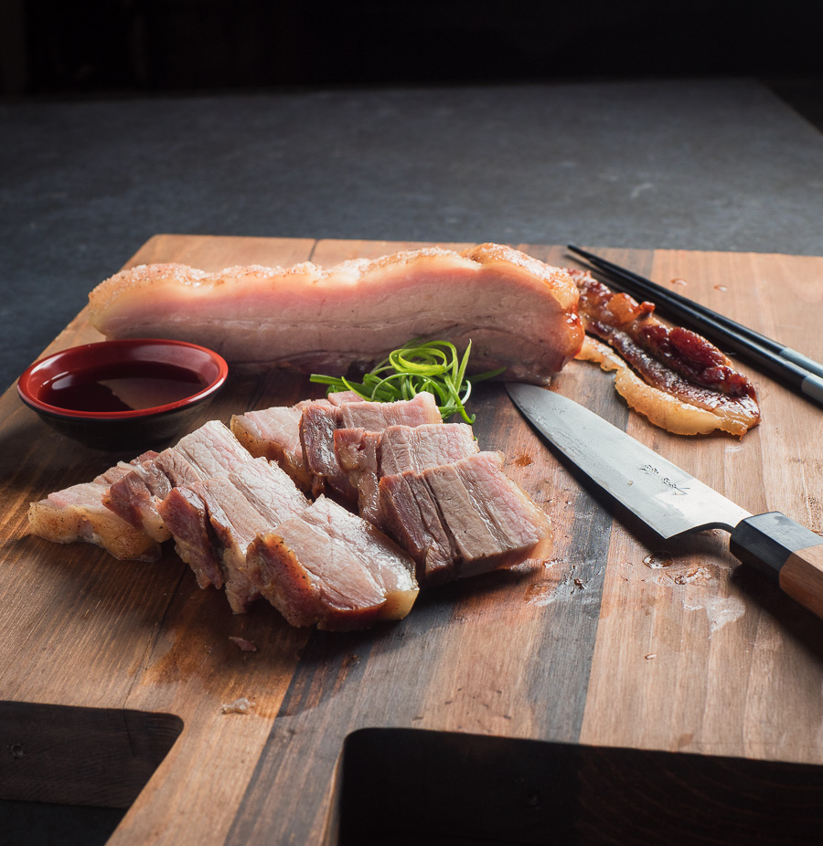 Momofuku pork belly sliced on cutting board with knife and chopsticks