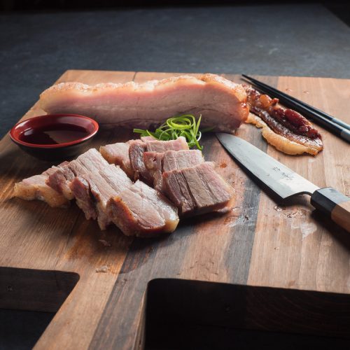 Momofuku pork belly sliced on cutting board with knife and chopsticks