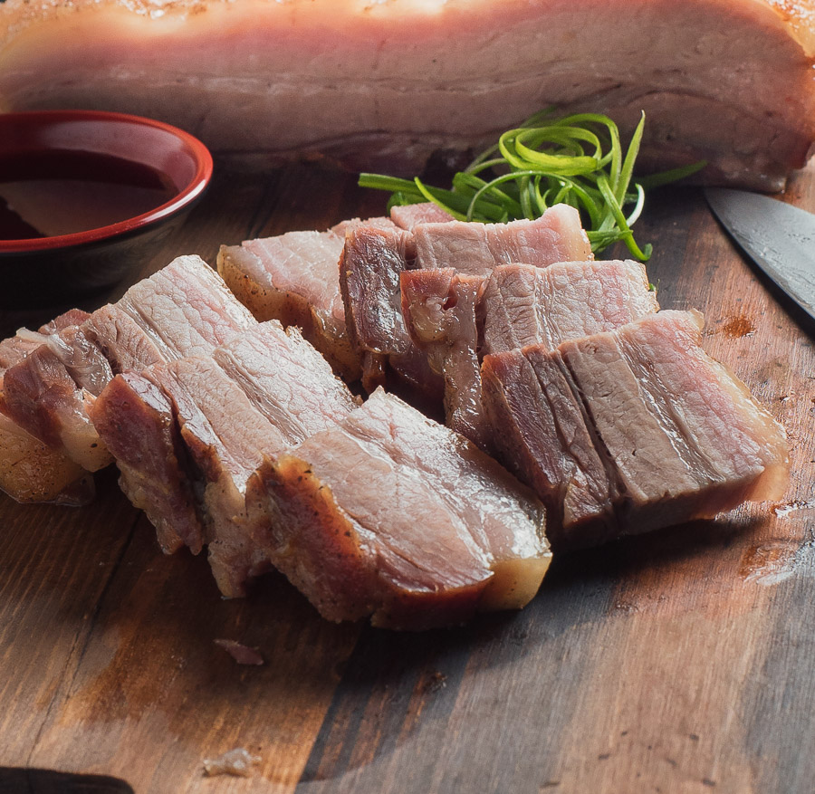 sliced pork belly on cutting board with knife and chopsticks