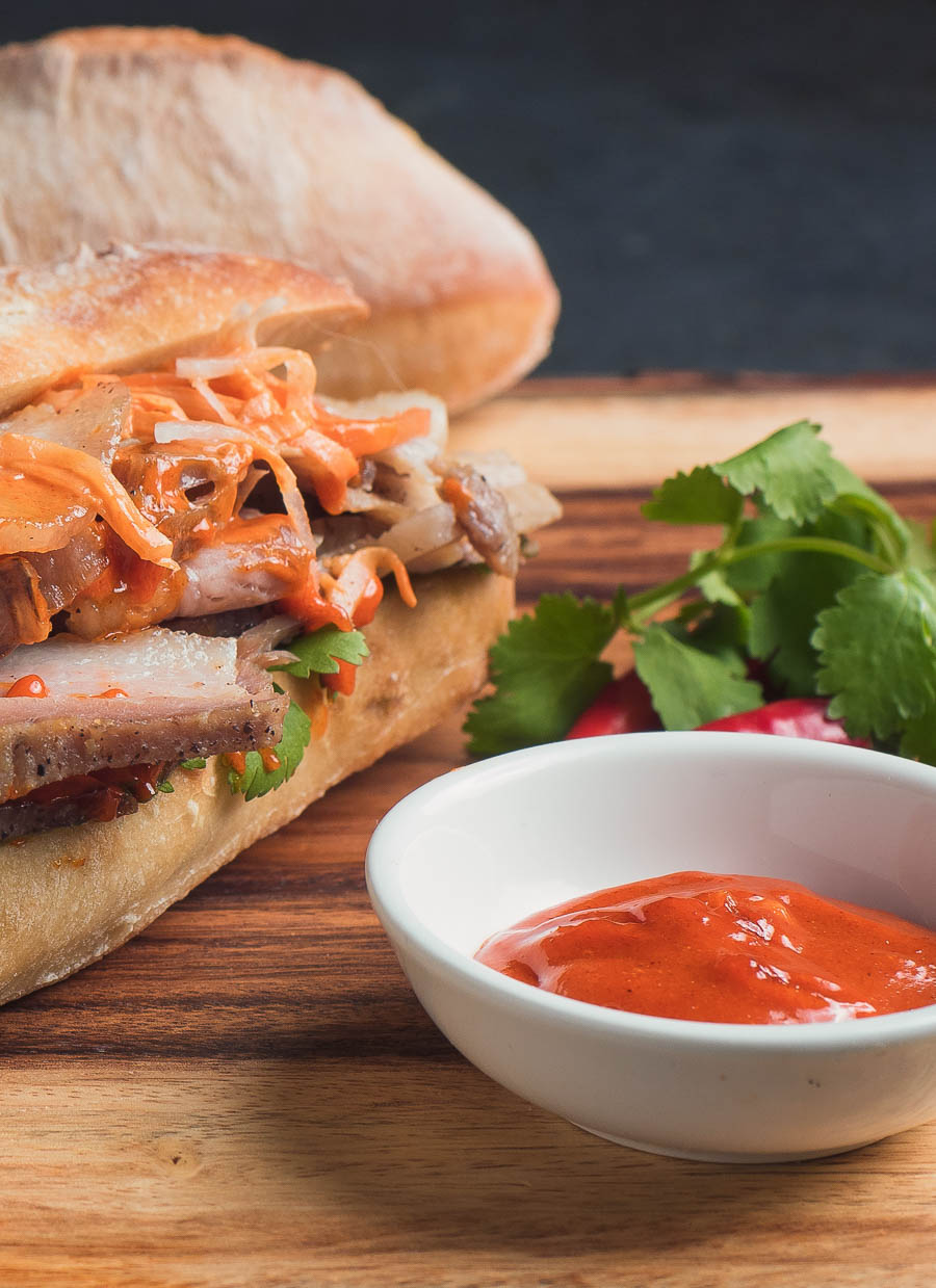 Gochujang mayonnaise in a white bowl next to a pork belly sandwich.