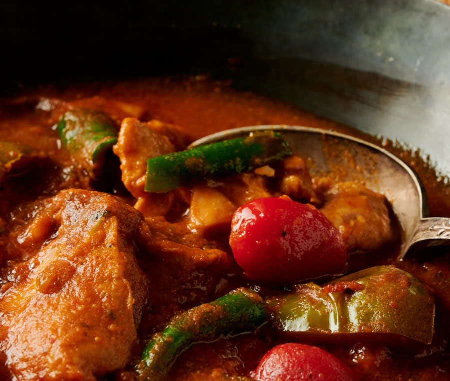 Close-up of chicken, chili and cherry tomato in red gravy.
