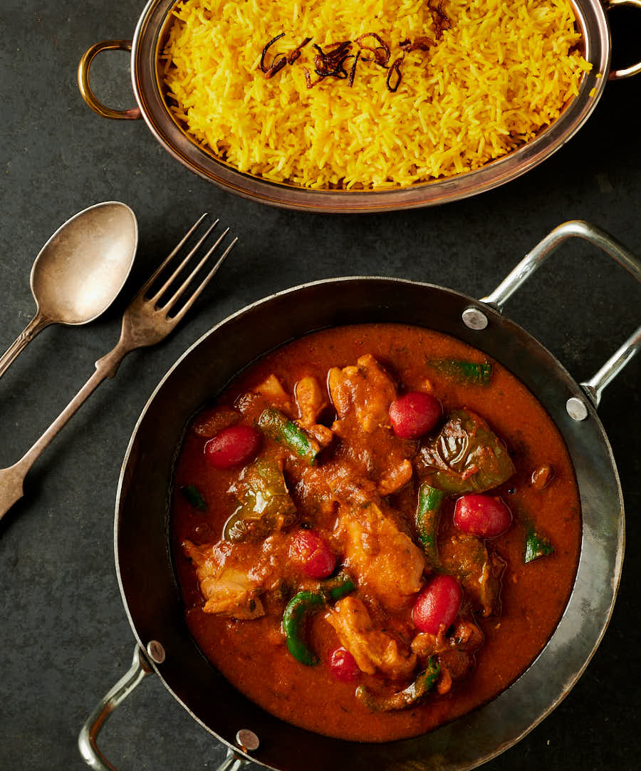 chicken jalfrezi in a kadai alongside a bowl of yellow rice pulao from above