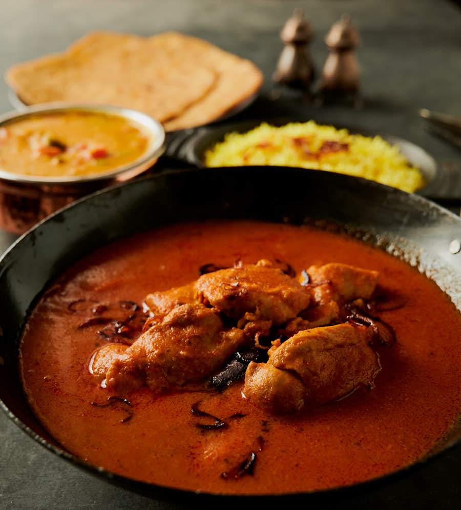 Chicken madras in a kadai with rice, parathas and dal from the front