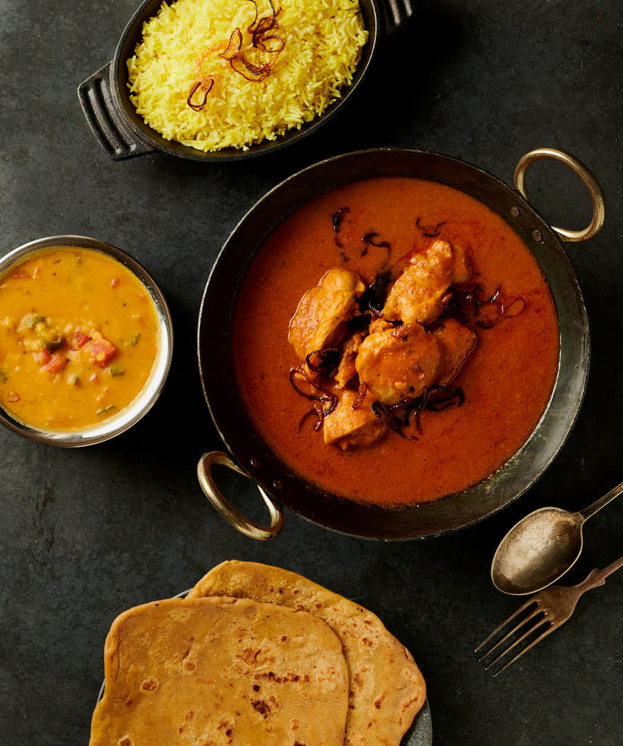 Table scene with chicken madras, parathas, dal and rice from above.