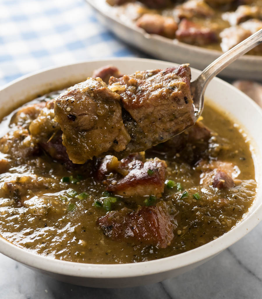 Spoon full of chile verde above a white bowl of chili.