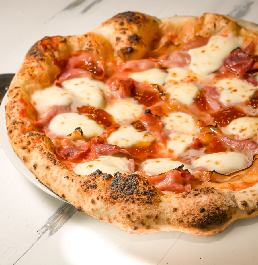 Proscuitto and fresh mozzarella Neapolitan pizza on a plate from the front.