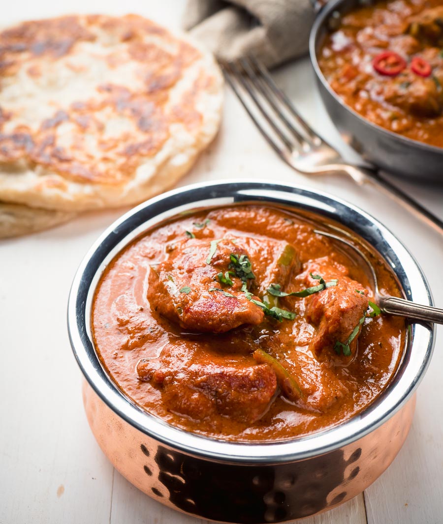 Restaurant butter chicken in a copper bowl with spoon.