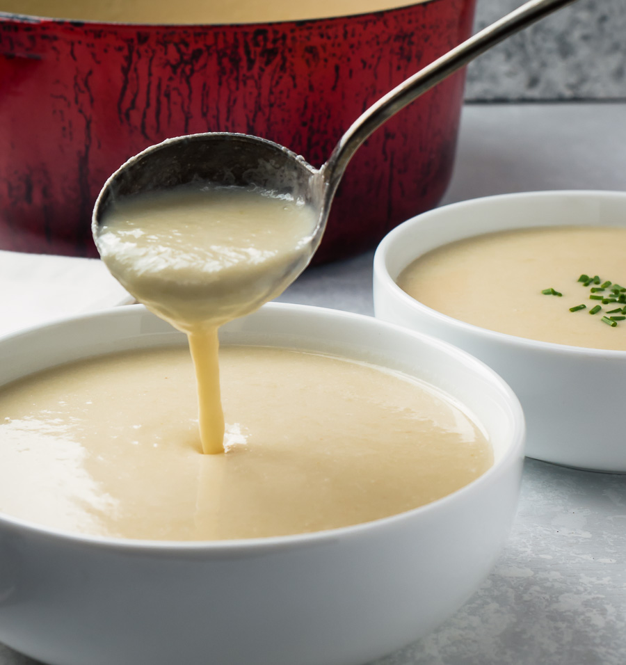 Ladling potato leek soup into a white bowl.