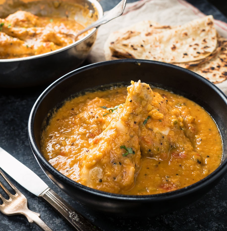 Chicken dhansak in a black bowl with paratha.