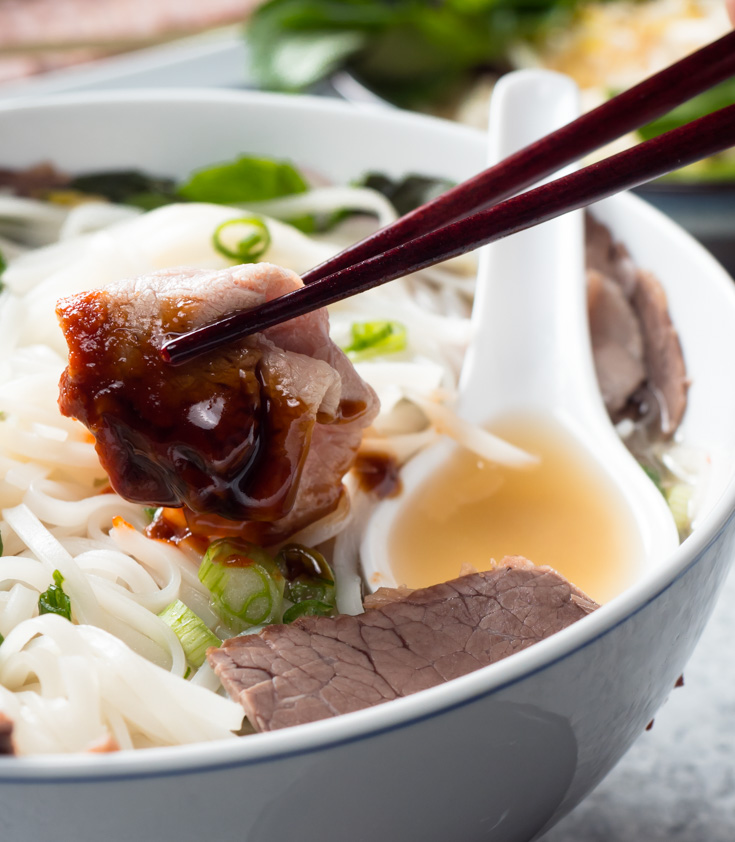 Beef slice dipped in hoisin held by chopsticks.