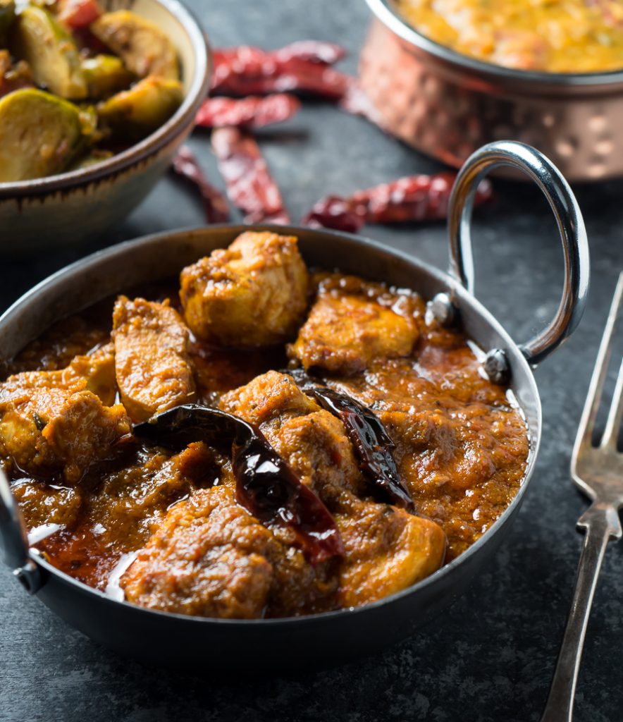 Chicken vindaloo with dried chili garnish in a metal bowl from the front.