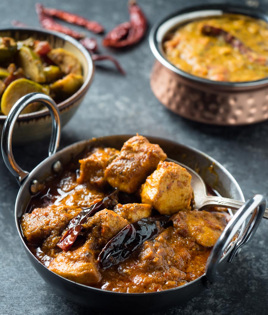 Serving chicken vindaloo from a metal bowl. Dal and vegetable curry in the background.