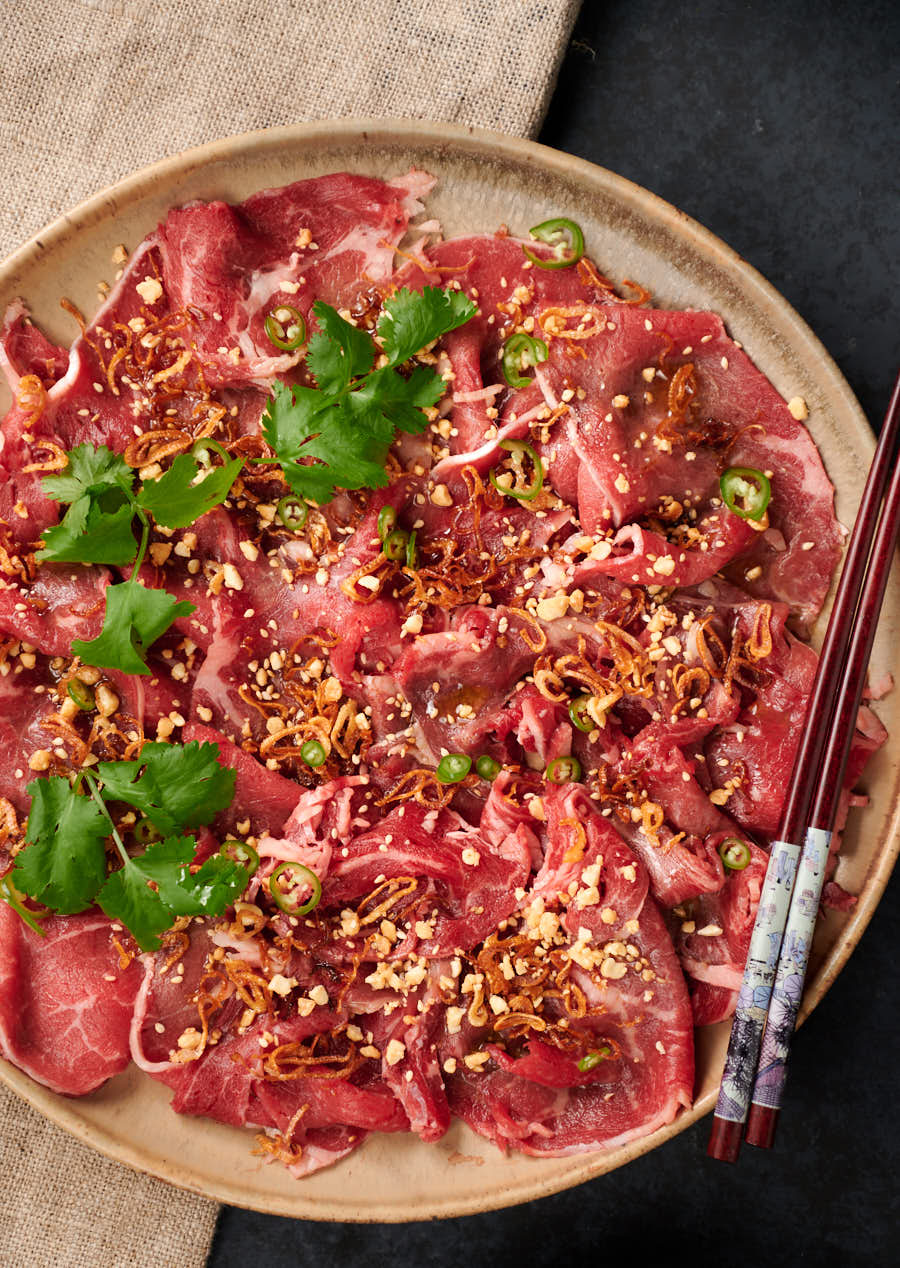 Platter of Asian style carpaccio garnished with sesame, peanuts, cilantro and green chili slices.