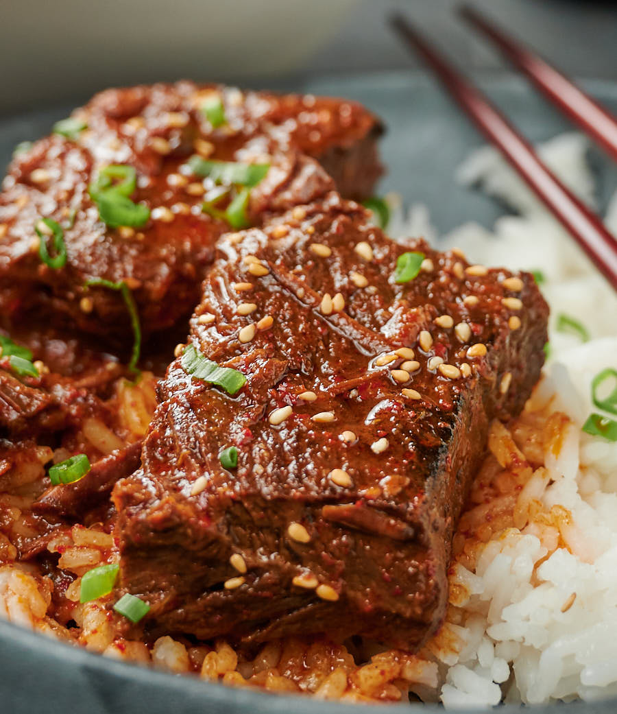 Close-up of two large pieces of Korean beef stew garnished with sesame seeds and green onions.