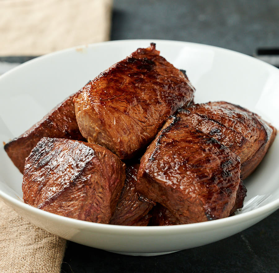 Large chunks of well browned beef in a white bowl.