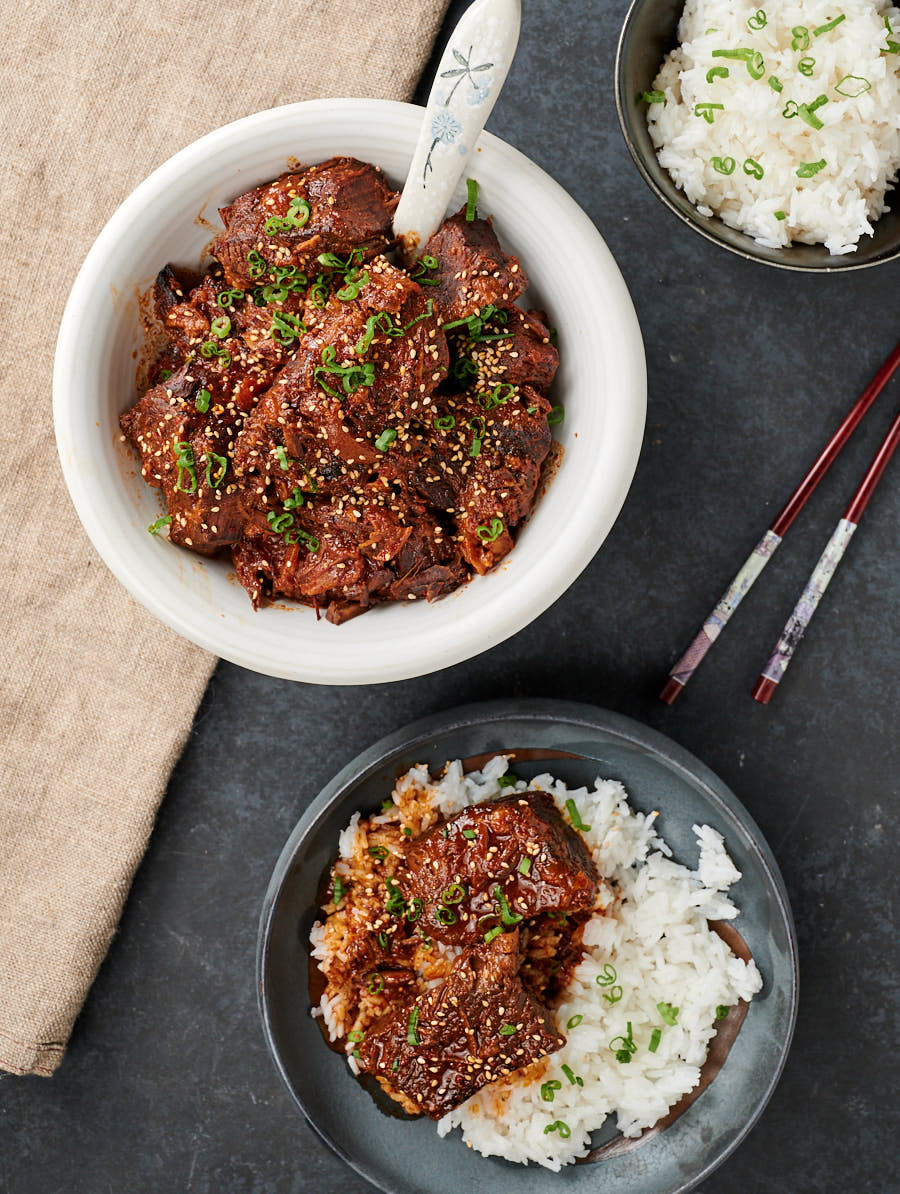 Scene with large bowl of Korean beef stew next to a plate with stew over rice.