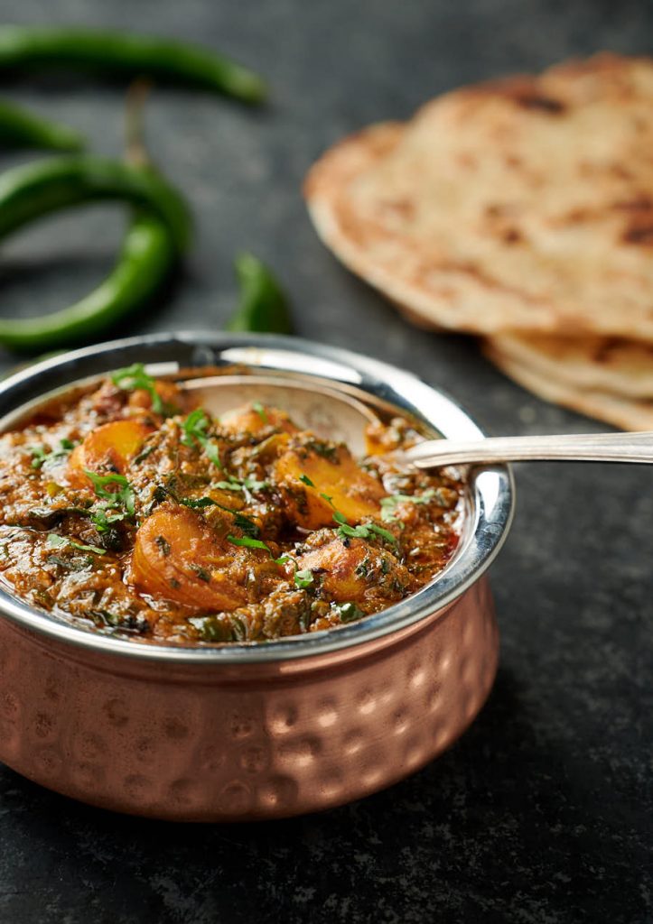 Saag aloo in an Indian copper bowl with spoon.