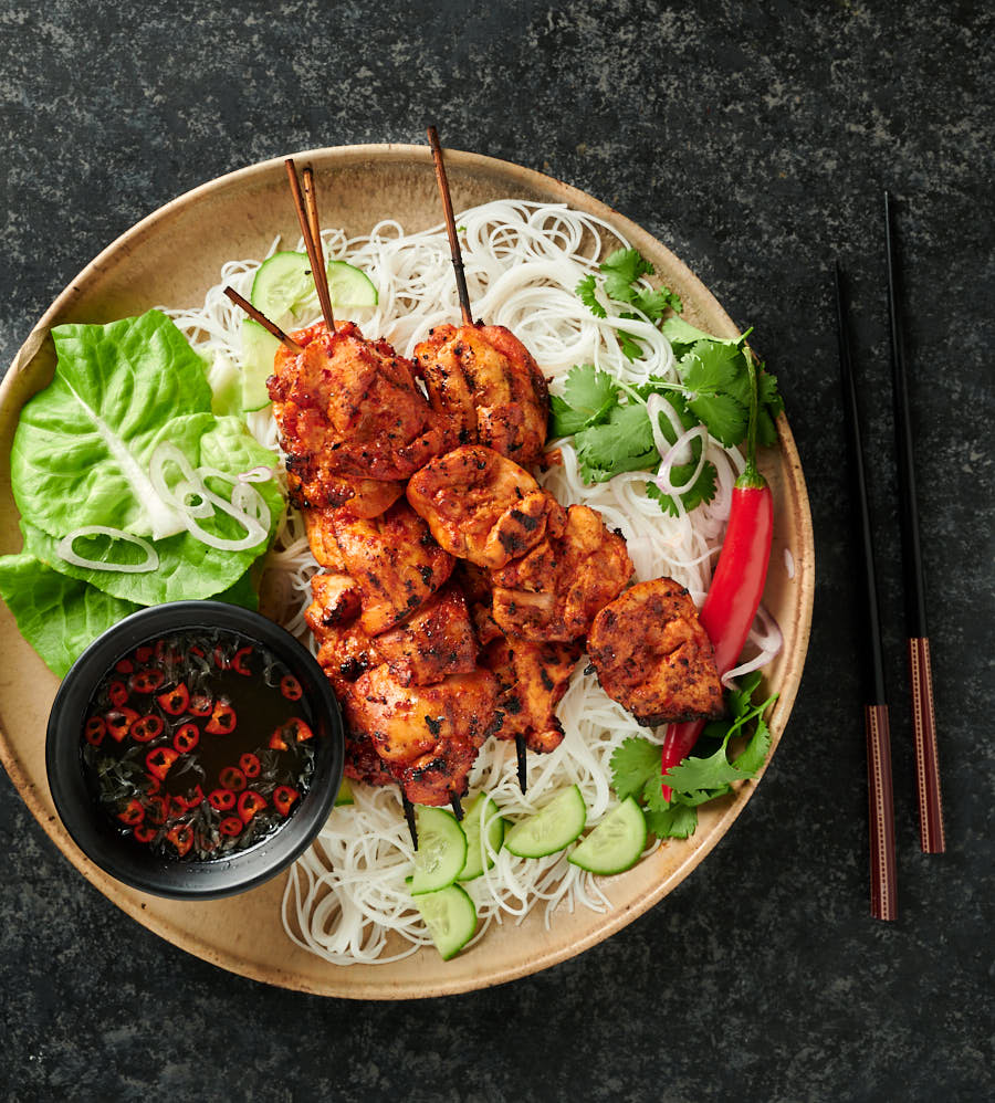 Spicy Korean chicken on a bed of rice noodles with nuoc Cham and garnishes from above.