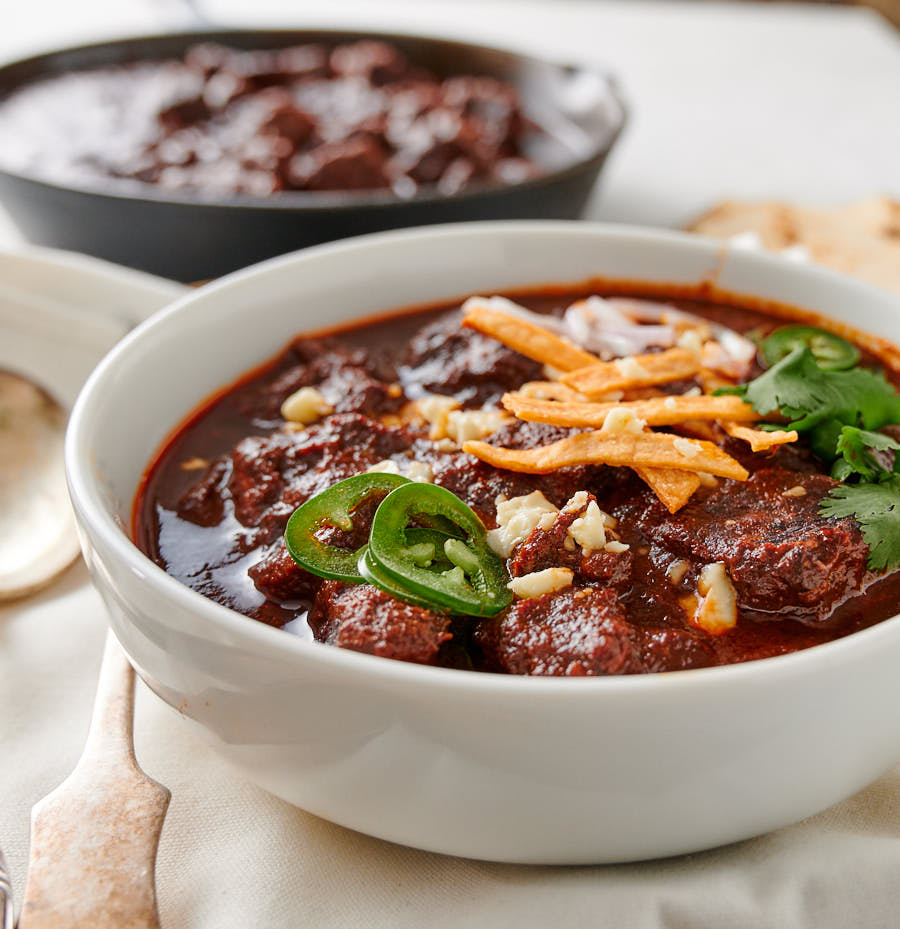 Chili colorado in a bowl garnished with jalapeño, tortilla strips and cotiija cheese.