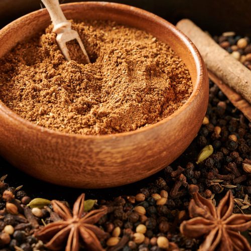 Bowl of garam masala surrounded by whole spices.