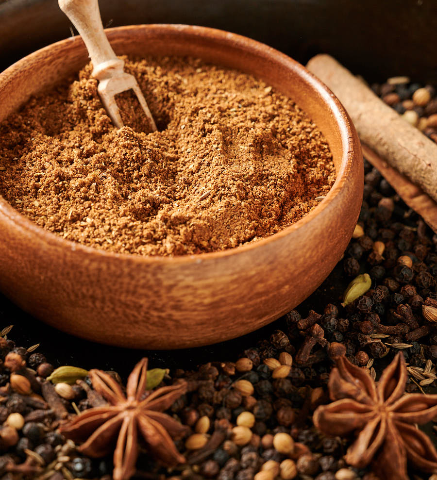 Bowl of garam masala surrounded by whole spices.