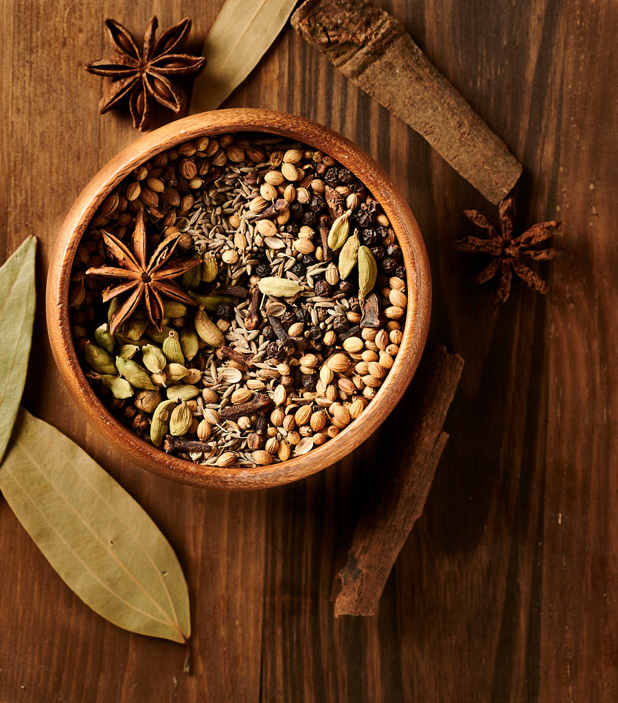 Garam masala whole spices in a small wood bowl from above.