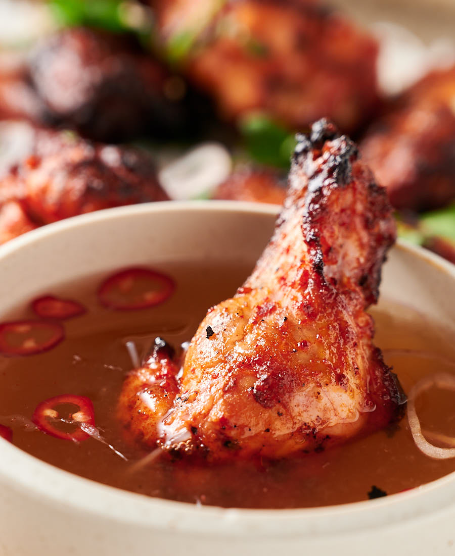 Close up of a Korean chicken wing in a bowl of nuoc cham.