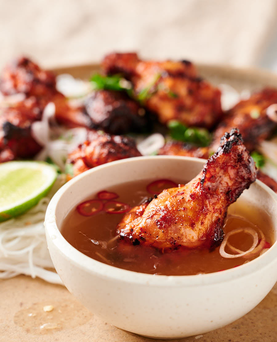 Korean chicken wing in a bowl of nuoc cham with a plate of wings in the background.