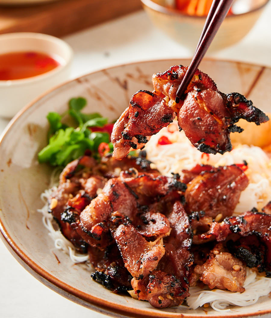 Grilled pork held in chopsticks above bowl of bun thit nuong