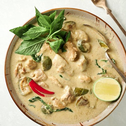 Thai green curry in a bowl with lime, Thai basil and red chili garnish from above.