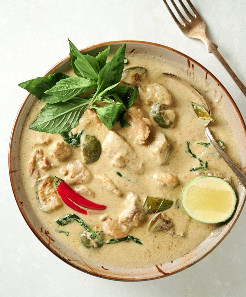 Thai green curry in a bowl with lime, Thai basil and red chili garnish from above.