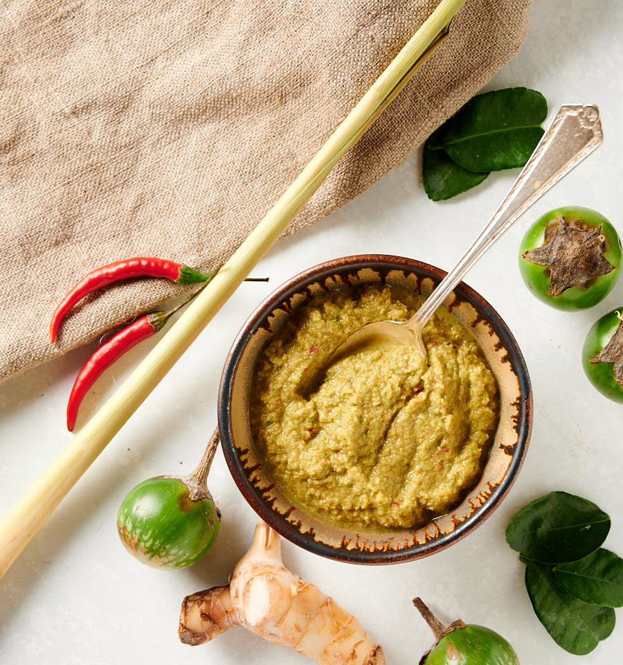 Thai green curry paste in a bowl surrounded by Thai curry ingredients.